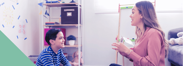 Speech-language pathologist sitting on floor of classroom with student. National Speech-Language-Hearing Month.